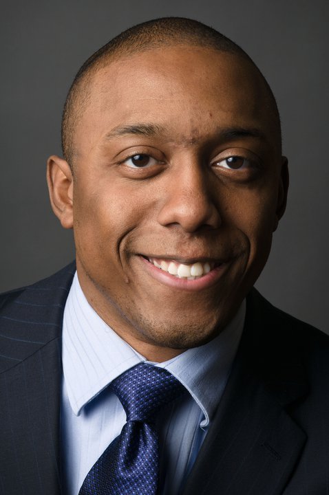 A professional photo of Chike Aguh smiling wearing a suit and tie.