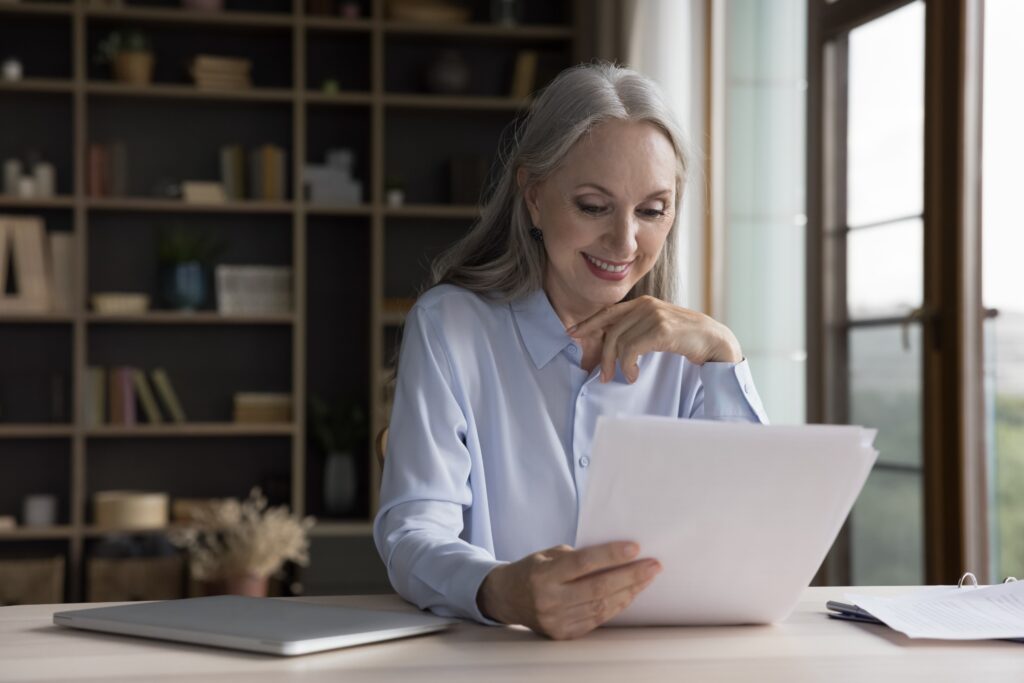 Happy mature caucasian business woman smiling while reading documents.