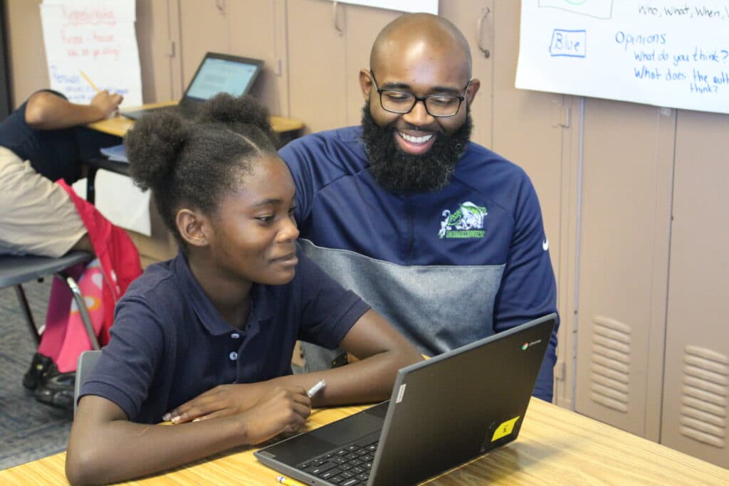 Darius Sawyers, former Fellow and principal at Paramount School of Excellence, smiles at a student working on her laptop.
