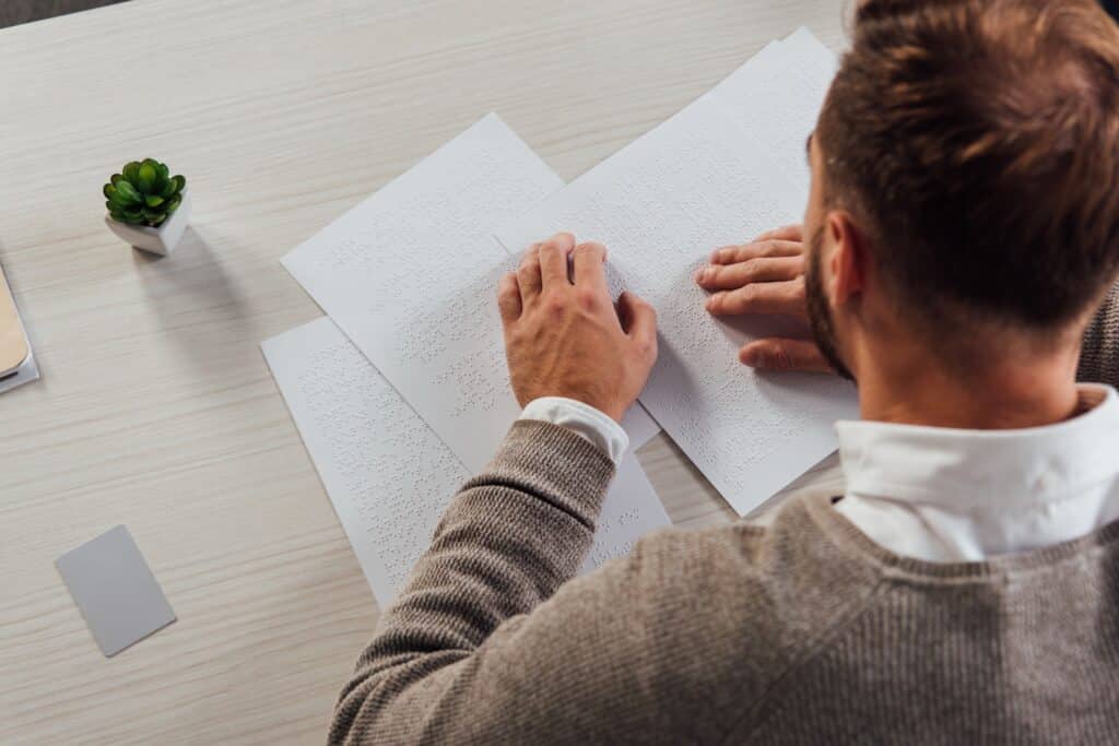 A visually impaired man sitting at a desk reading documents in Braille.