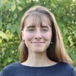 Anne Seefeldt, Project Associate and Ruckelshaus Fellow at Meridian Institute, wearing a blue shirt and smiling for a photo in front of green bushes