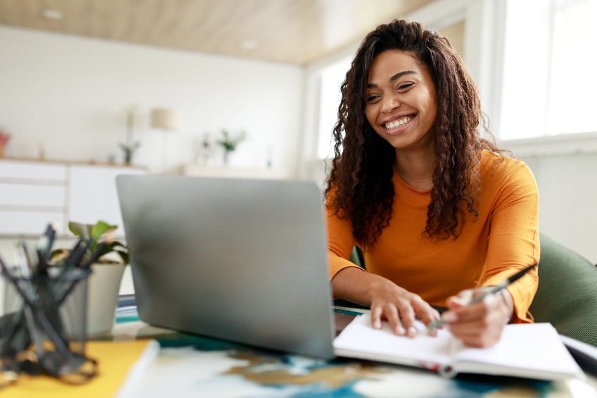 Young African American woman sitting at her desk using a computer and writing in a notebook