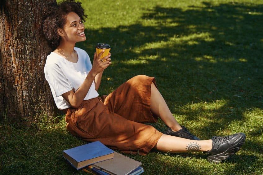 Female grad student relaxing under a tree with coffee and her books