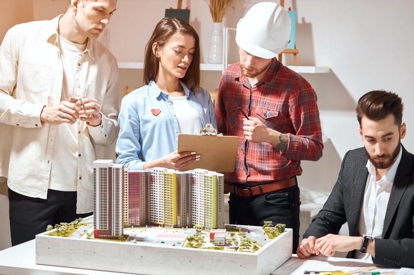 Female architect reviewing a 3D model and discussing plans for developing a high-rise with three male colleagues