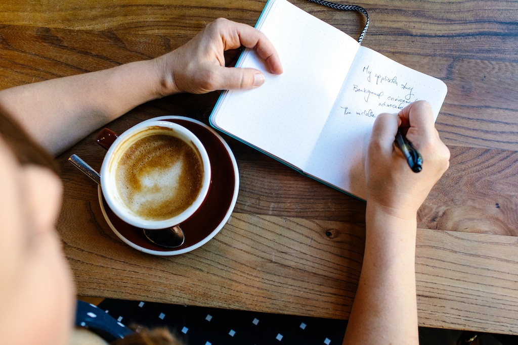 On overhead view of Dr Vicki Johnson writing in a notebook with a latte at a coffee shop