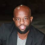 HBCUvc Fellow Terrence Battle smiling for a professional portrait wearing a black suit and black and white striped shirt