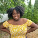 Headshot of Serina Gousby smiling at camera in yellow shirt. 