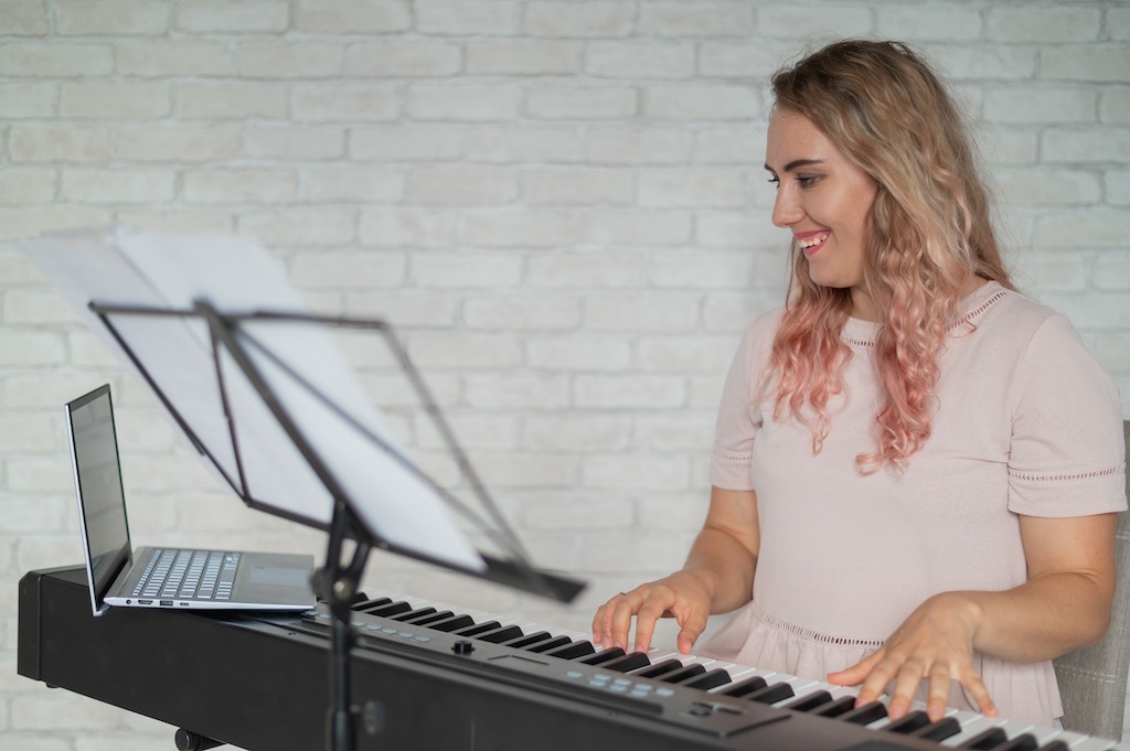White female composer with blond hair and pink ends playing a keyboard and composing music. 
