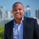 Terik Tidewell headshot smiling while wearing light blue dress shirt and navy suit