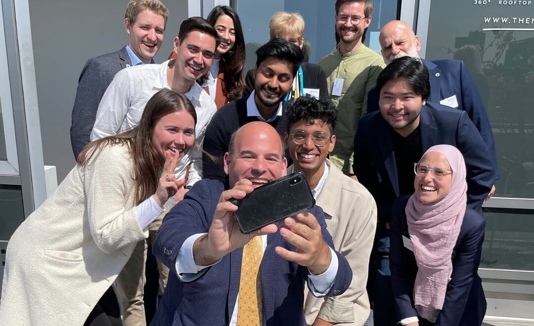Tyler Pugeda, 2022 Fulbright Germany Fellow, smiling for a picture with eight 2022 Fulbright Germany Fellows, Fulbright Germany staff, and Deputy Assistant Secretary, Ethan Rosenzweig 