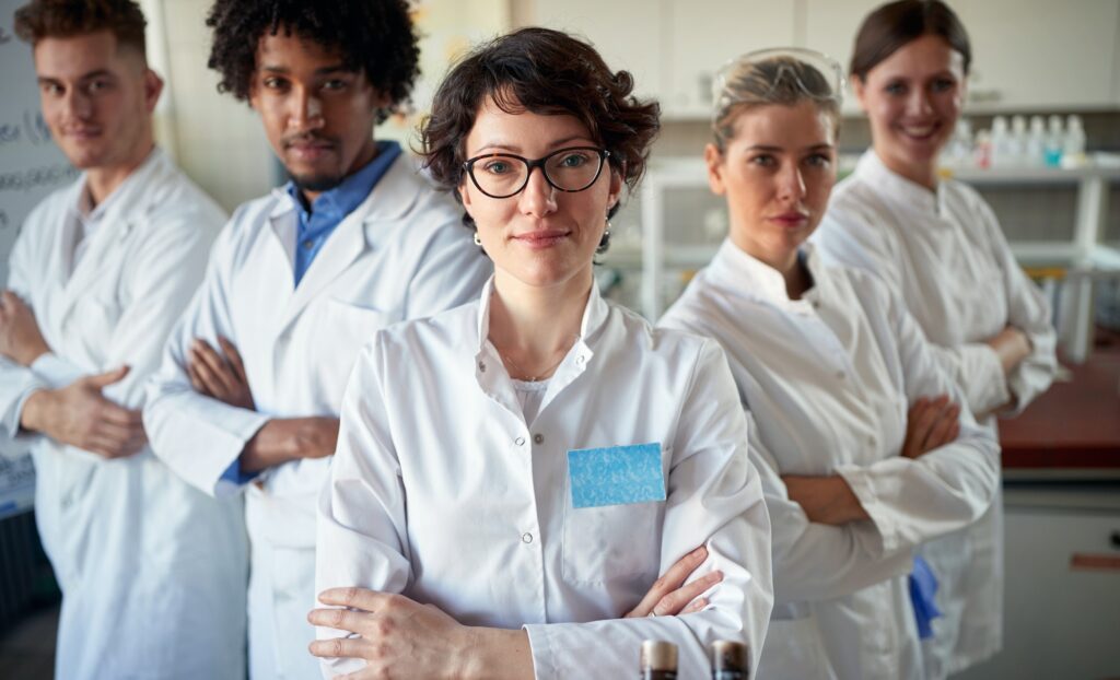 Diverse team of female and male experienced researchers wearing white lab coats in a lab.