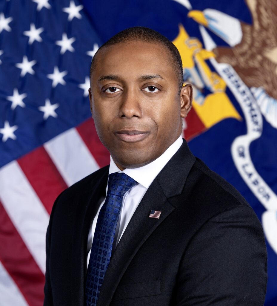 Chike headshot in front of American flag wearing black suit