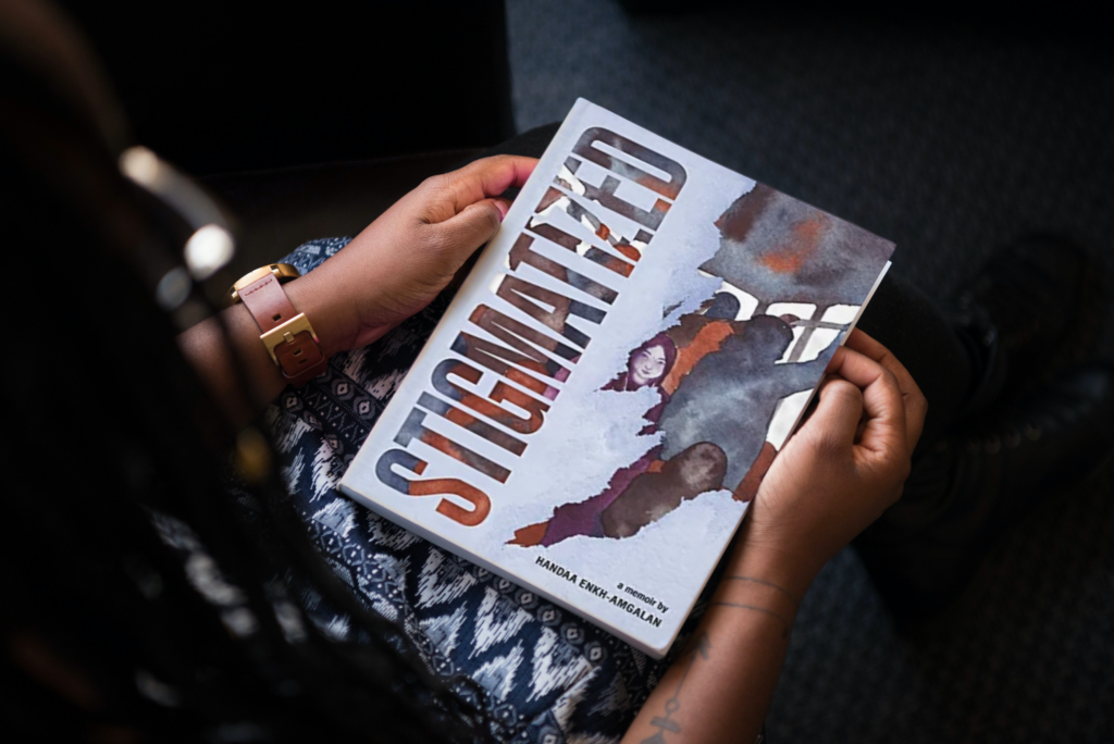 An African American woman holding a copy of the book Stigmatized by Handaa Enkh-Amgalan.