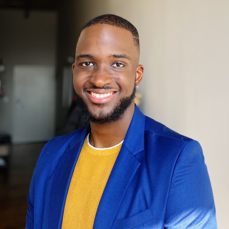 Trevaughn Latimer smiling in a professional photo wearing a blue suit jacket and yellow sweater.