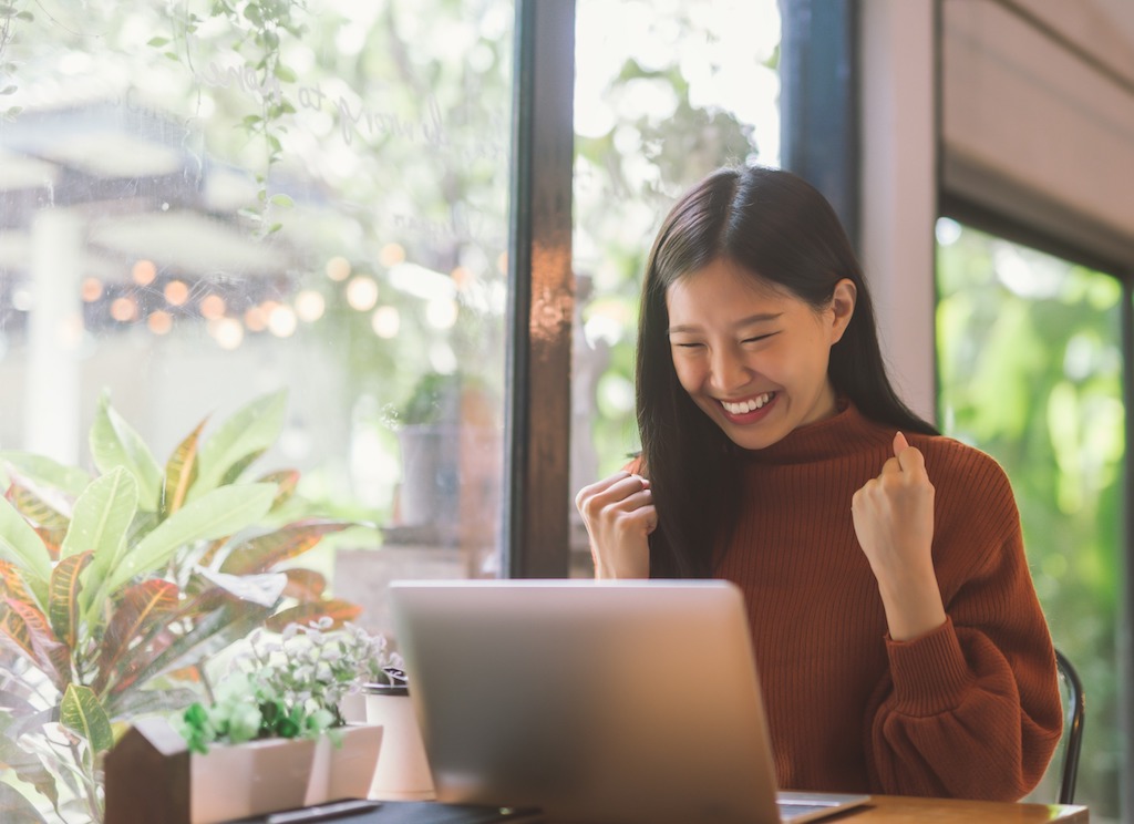 Young Asian woman celebrating success earning an interview after submitting a great cover letter, resume, and application for a fellowship.