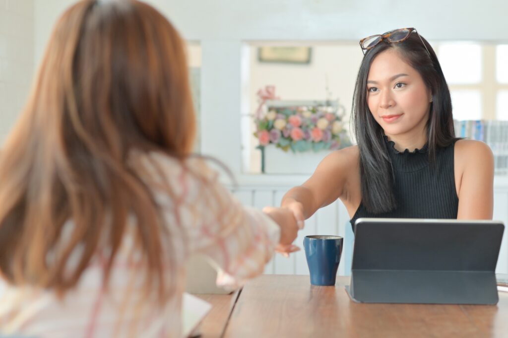 A portrait of a young female hiring manager shaking the hand of a female job candidate before an interview.