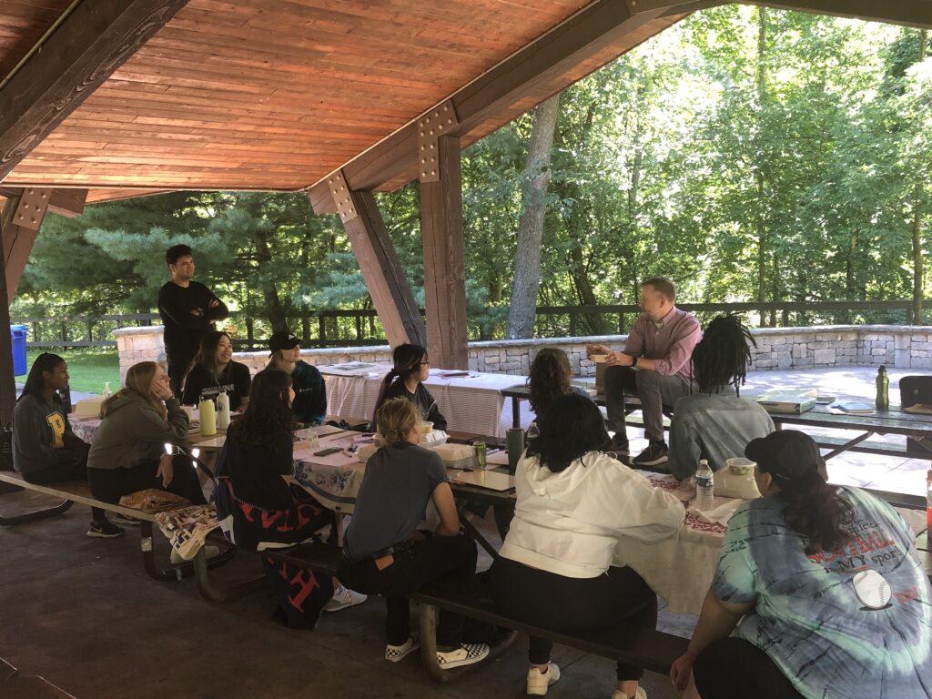 Cleveland Public Service Fellows sitting at a canopied table outdoors watching a mentor speak