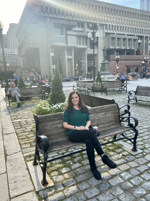 Dr. Vanessa Vieites sitting in a public bench in a courtyard near Faneuil Hall Marketplace in Boston, Massachusetts, while on her AAAS Mass Media Science and Engineering Fellowship.