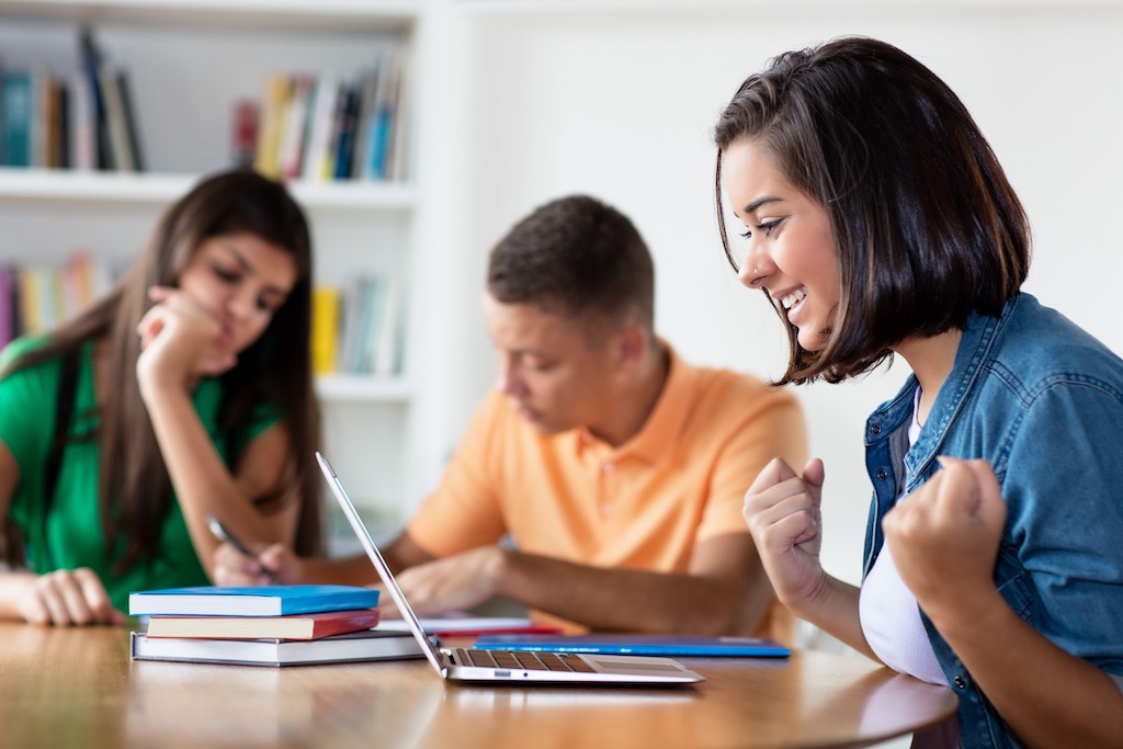 Fellowships for DACA recipients provide funding and unique experiences for students and professionals. Pictured is a female student and DACA recipient celebrating after receiving positive news while working with group of students at the library.