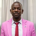 A professional photo of Public Service Emerging Leaders Fellowship winner Jacob De' Kiage. In the photo Jacob is wearing a pink suit, white shirt, and a red tie.