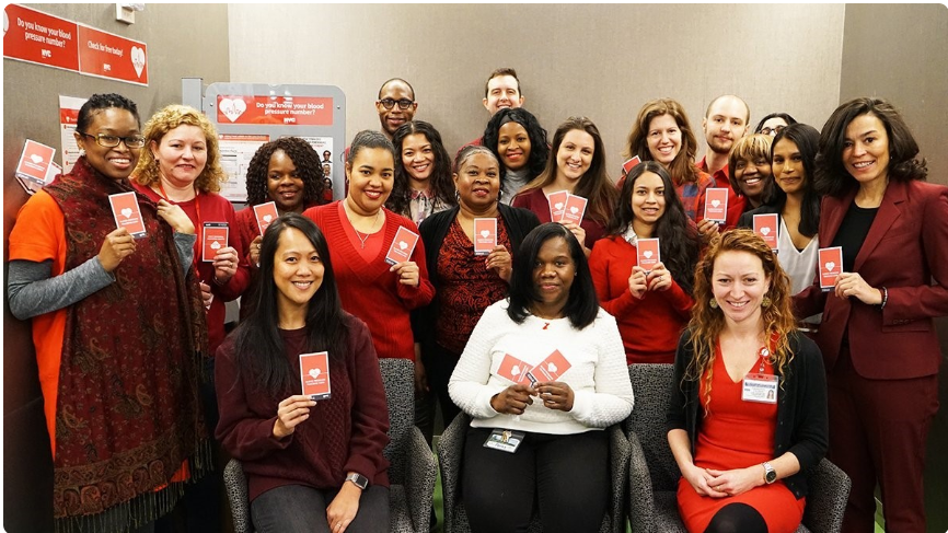 Group photo of Dr. Ayanna Vasquez, recipient of a fully funded preventive medicine residency, with the option to pursue a fully funded MPH, at the University of Wisconsin-Madison, standing on the left most side with her colleagues from the NYC Department of Health and Mental Hygiene. Everyone is holding up a little red card that says "Do you have your blood pressure number?"