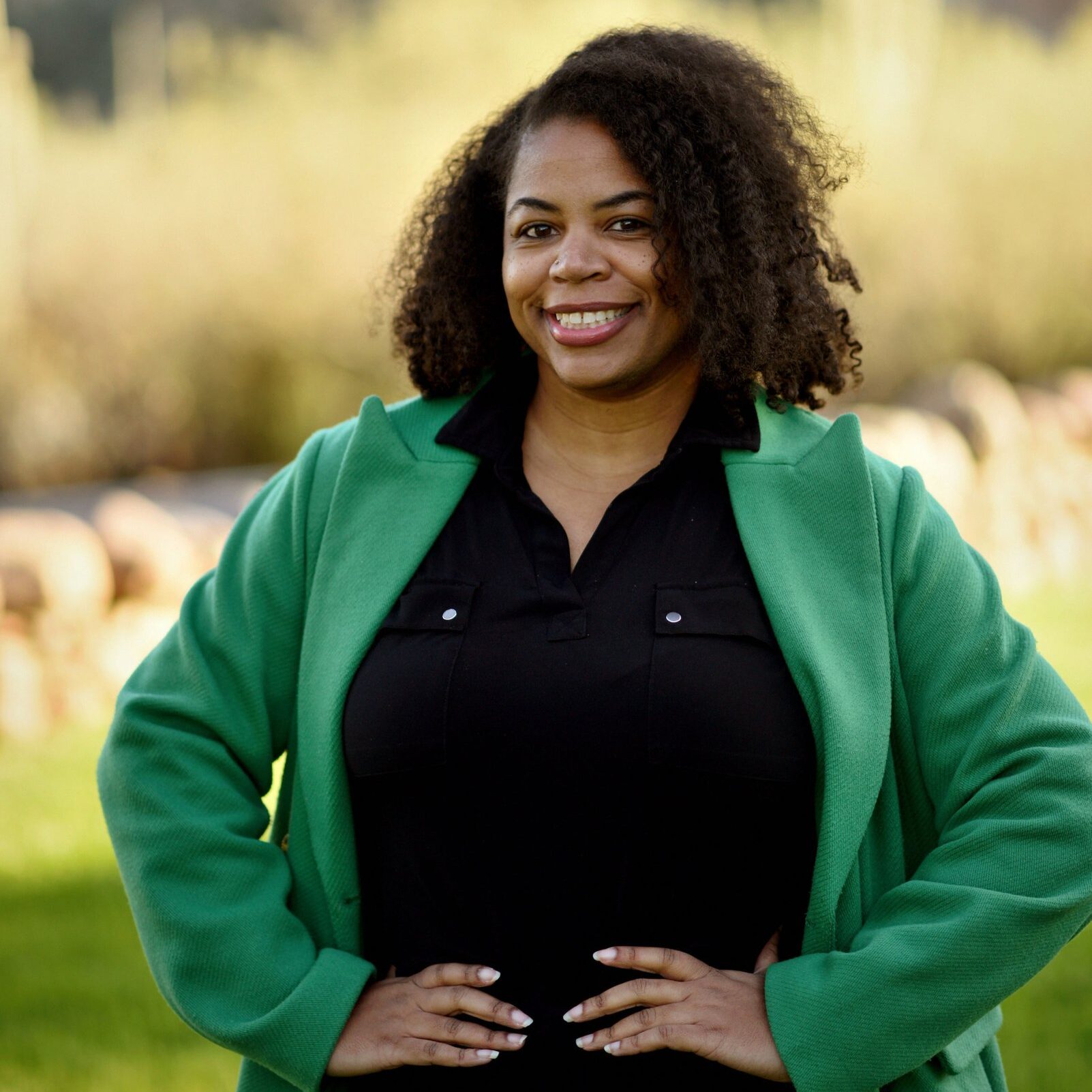 Jackie McKinney standing with her hands on her side, posing in front of lush green landscape.