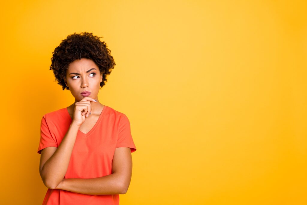 Beautiful young african american woman pondering the answer to a question while standing in front of a vibrant, yellow background.