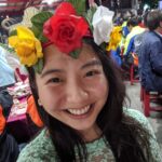 Sunny Huange, Fulbright ETA in Taiwan, smiling for a close up photo wearing a crown filled with yellow, red, and white flowers.