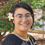 Natalia Fareti smiling for a professional photo with a white flower in her right ear.