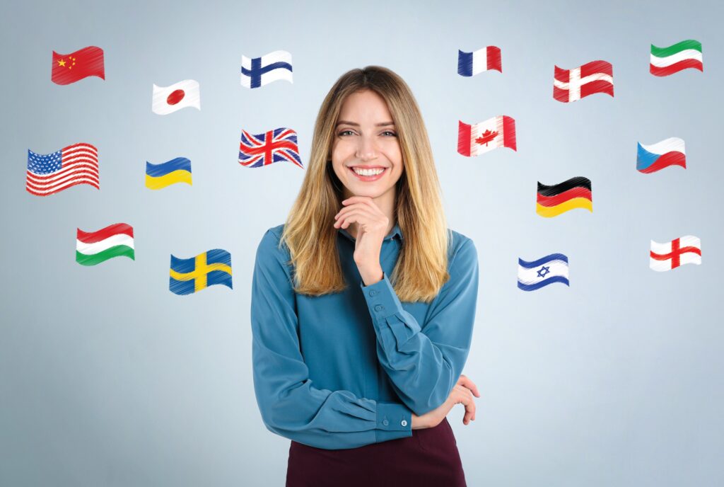 Smiling young woman standing in front of a background with myriad country flags symbolizing the many countries one can do a Fulbright U.S. Student Award and Fulbright U.S. Scholar award in.