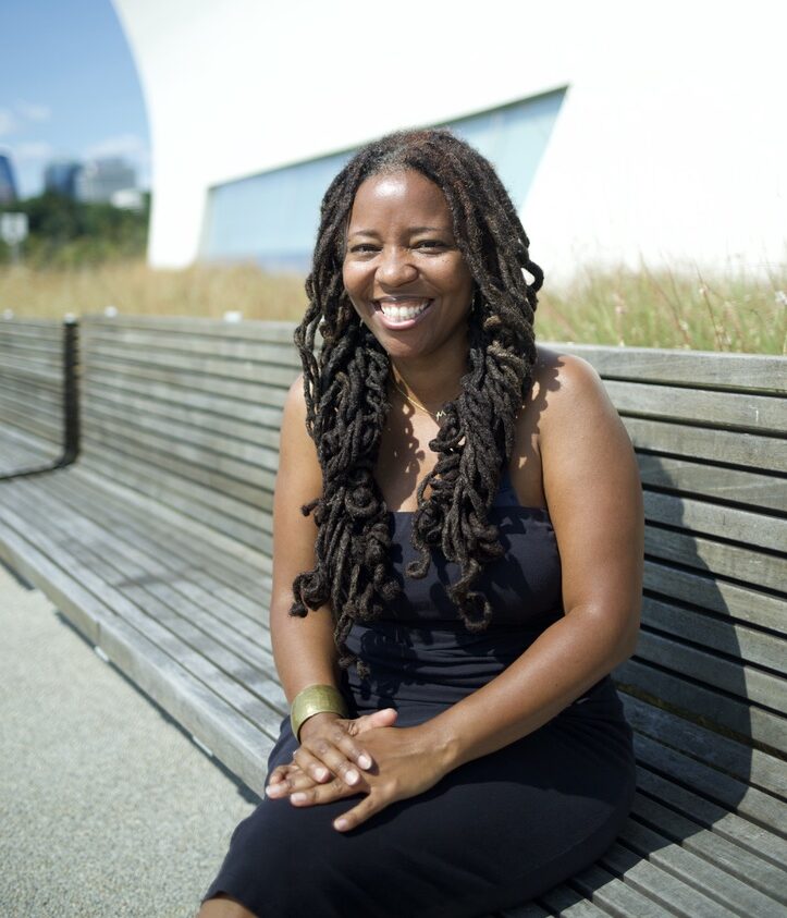 Dr. Mi'Jan Tho-Biaz sitting outside the Kennedy Center on a park bench. She is wearing a black dress, hands crossed over her leg with a forward facing smile