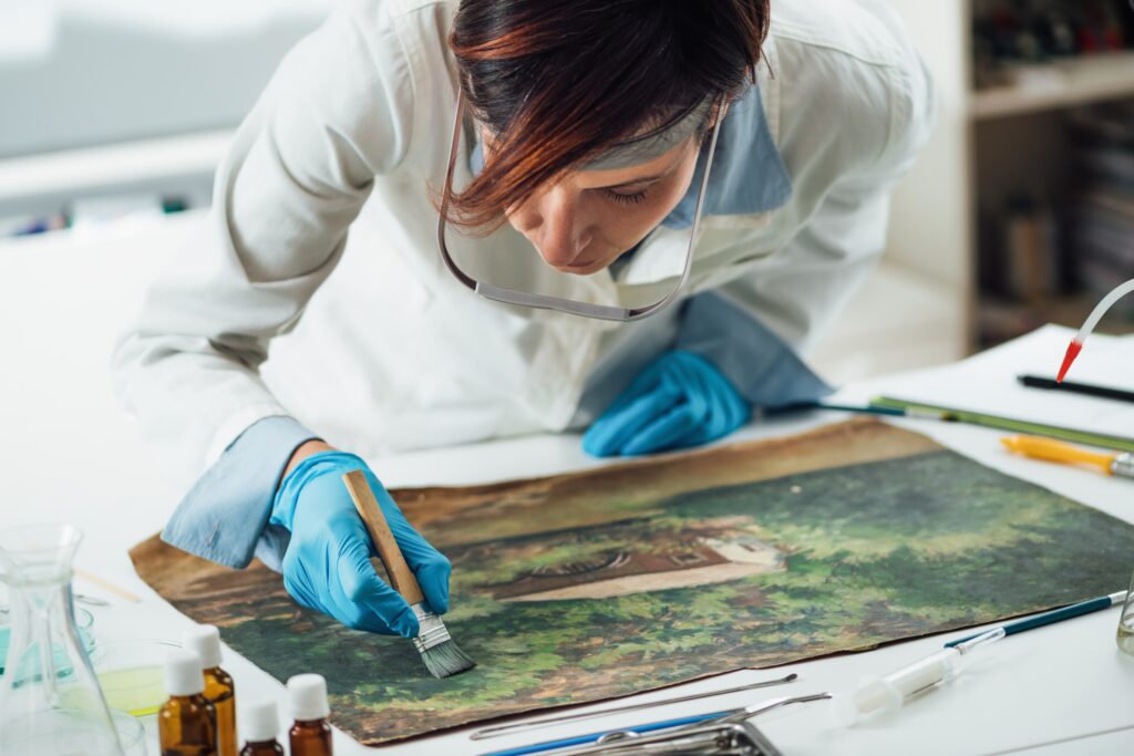 Young female conservator restoring an old oil painting by removing varnish.