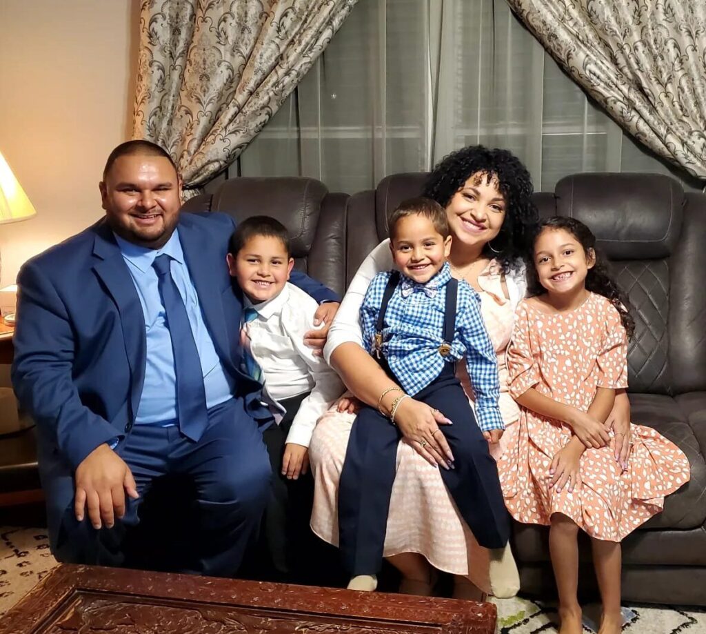 Global Health Corps Fellow Paris Acosta and her family. From left to right: husband Alex and children Cameron, Kylo on Paris’ lap, and daughter Khloe. The boys and their father are wearing matching blue formal wear. Paris and her daughter are wearing matching pink-peach colored dresses.
