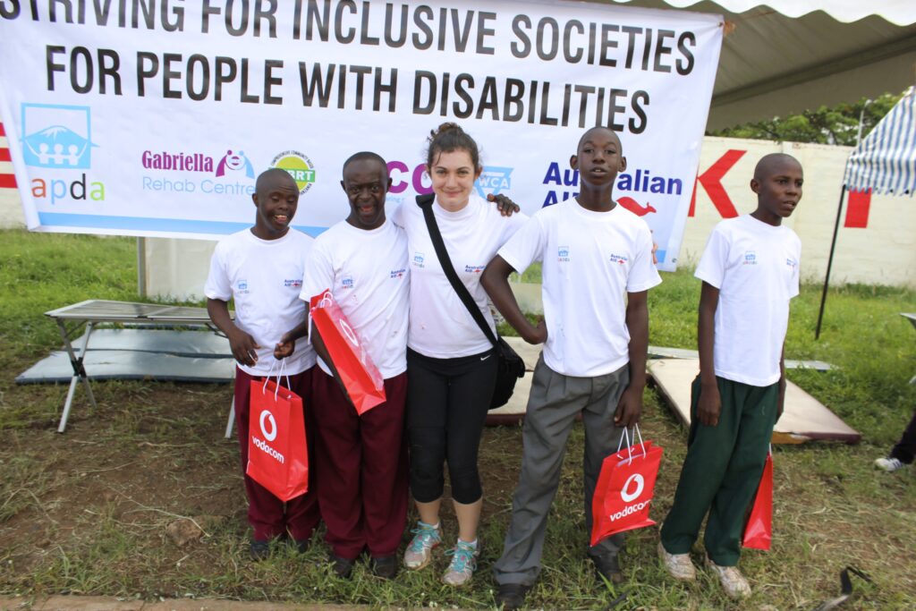 Meghan stands with four young Tanzanian teens in front of a banner that says "striving for inclusive societies for people with disabilities"