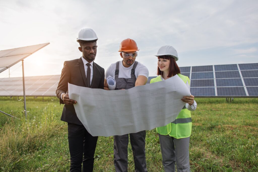Two engineers and one technician examining drawings together while standing outdoors, engineering a clean energy solar farm.