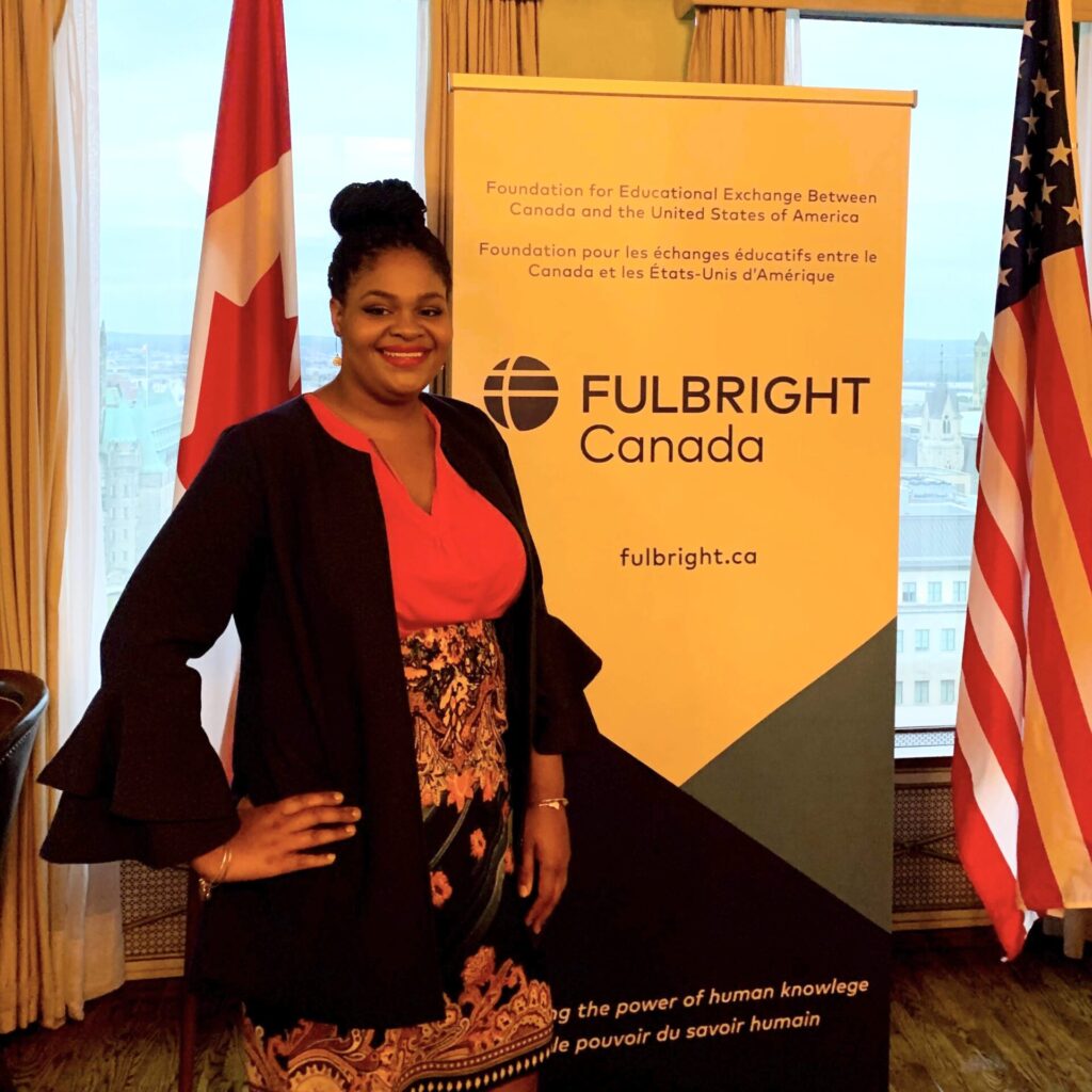 Brittany Christian at the opening reception for Fulbright Killam Fellowship participants in Ottawa, Canada. She stands in front of a banner that reads Fulbright Canada, wearing a red dress with a black suit jacket.