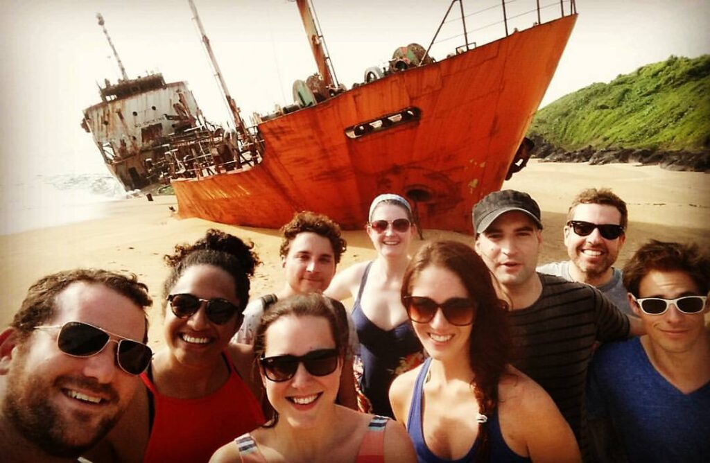 Will stands with a group of his colleagues in Liberia with an old shipwreck in the background.