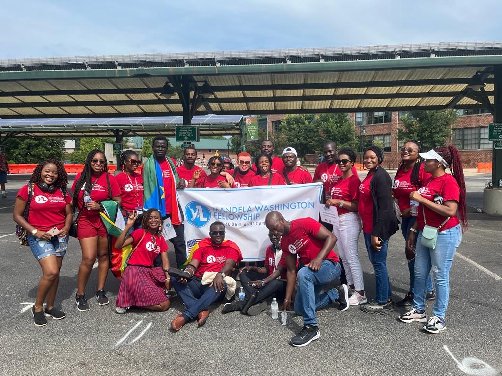 Daniel Adama with his Mandela Washington Fellowship cohort. The group of people are wearing a red shirt with the fellowship's logo, and two people hold a white and blue banner that reads, "Mandela Washington Fellowship."