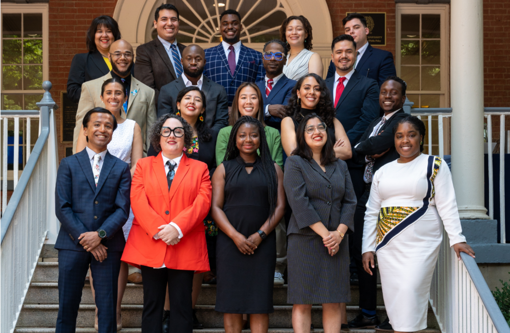 Apply Now to The 2024 National Urban Fellows Program. Rows of Fellows or various ethnicities, dressed in business professional attires, standing on a large staircase at the entrance of a building.