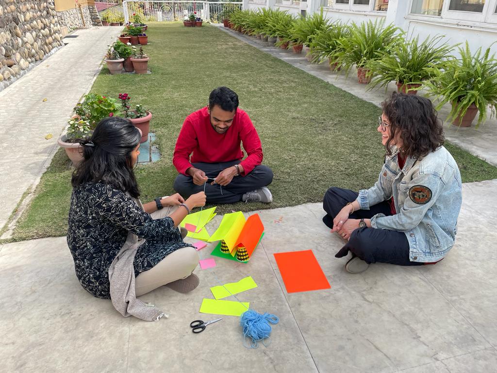 Erin sits with two Senior Fellows in an outdoor setting, with some colorful creative items spread on the ground between them.