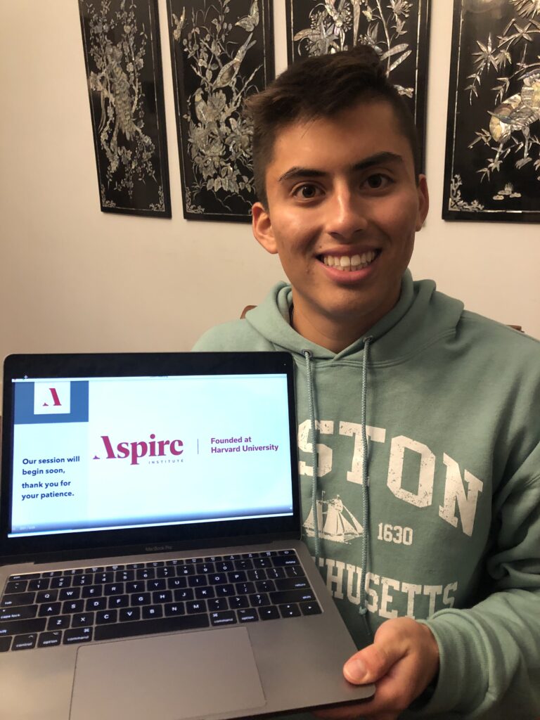Bryan Zapata grins at camera, showing the laptop screen that signals he finished the Aspire Leaders Program