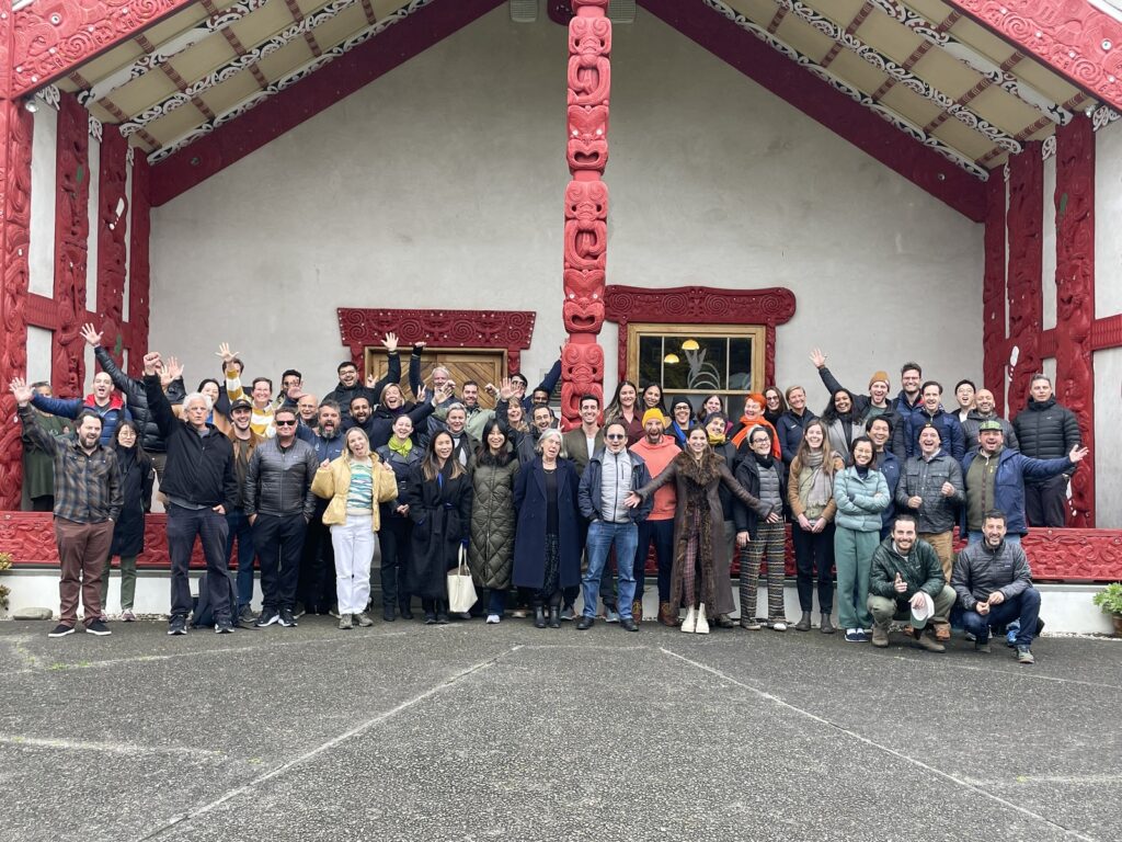 Group photo of Edmund Hillary Fellows standing in front of a bright red Maori building decorated with painted designs and sculptures.