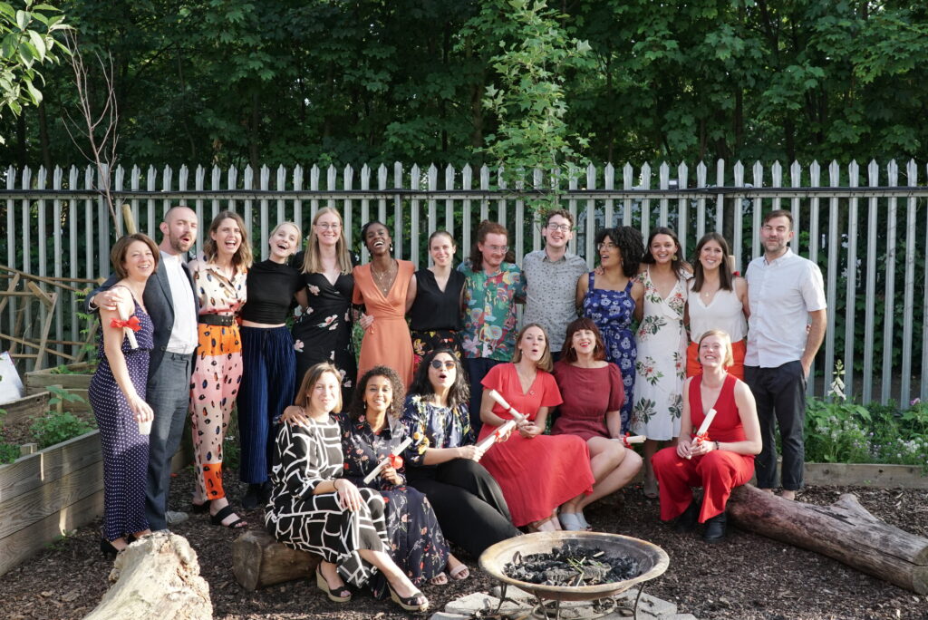 A group of Year Here fellows, and mulit-fellowship winner Ruth Martin, formally dressed stands in a semi-circle around a fire-pit for a group photo.
