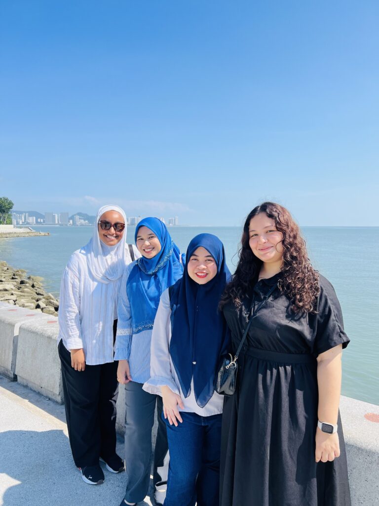 Layan and three other women stand for a group photo with the sea and blue sky visible behind them.