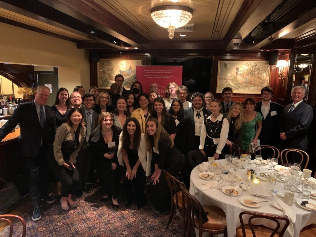 Fulbright Killam Fellow Anusha Natarajan posing with many other students in a dimly lit restaurant. A table with white tablecloth is seen on the right hand side.