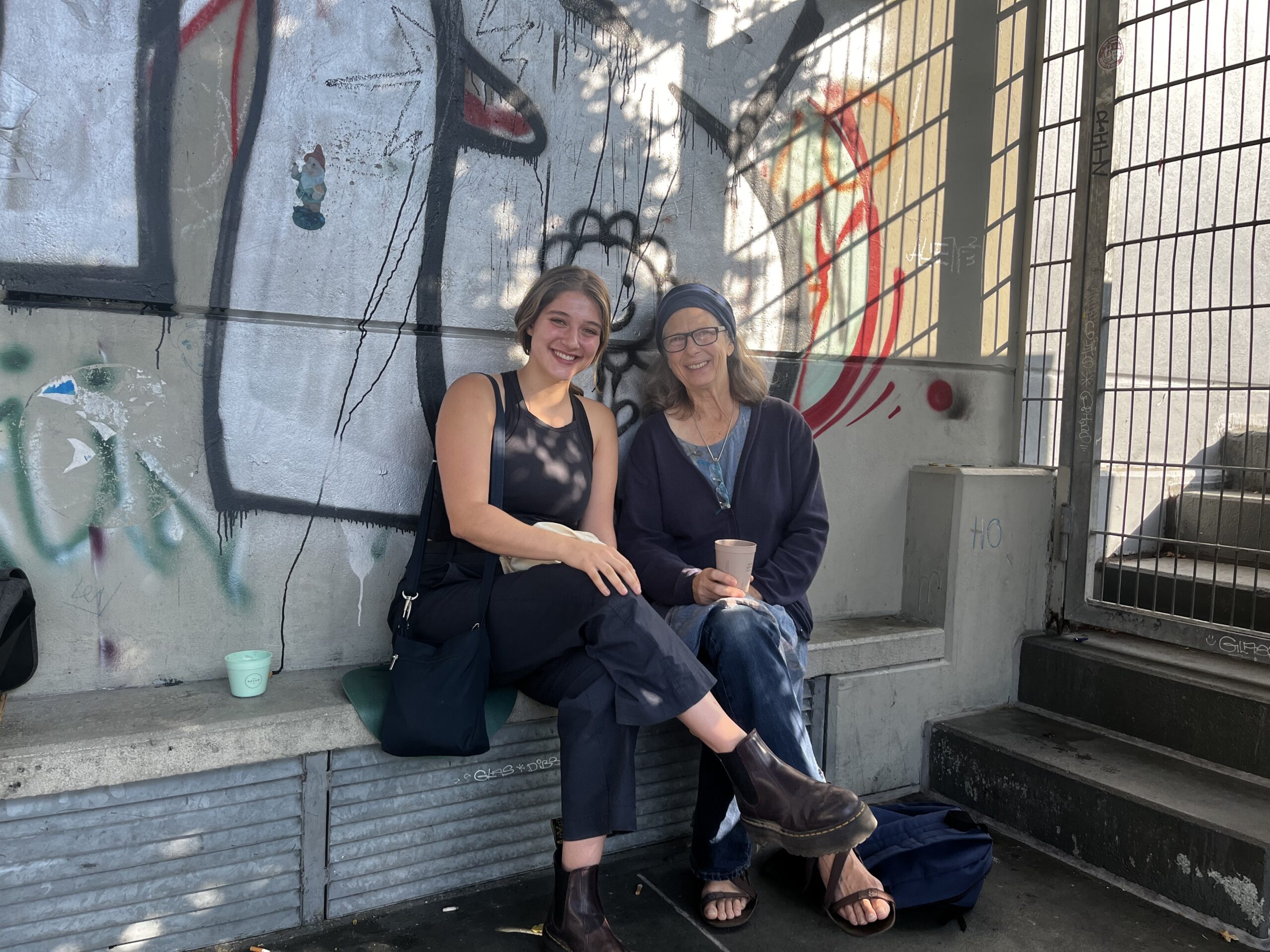 Eden Brockman sits with her host mom in Germany on a concrete bench with graffiti on the wall behind them.
