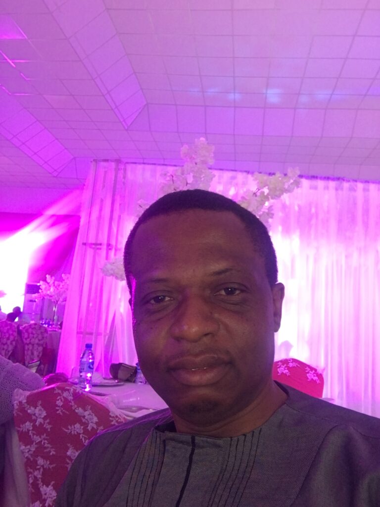 A close up Chinedu at an indoor venue with bright pink lights, lightning up the background.