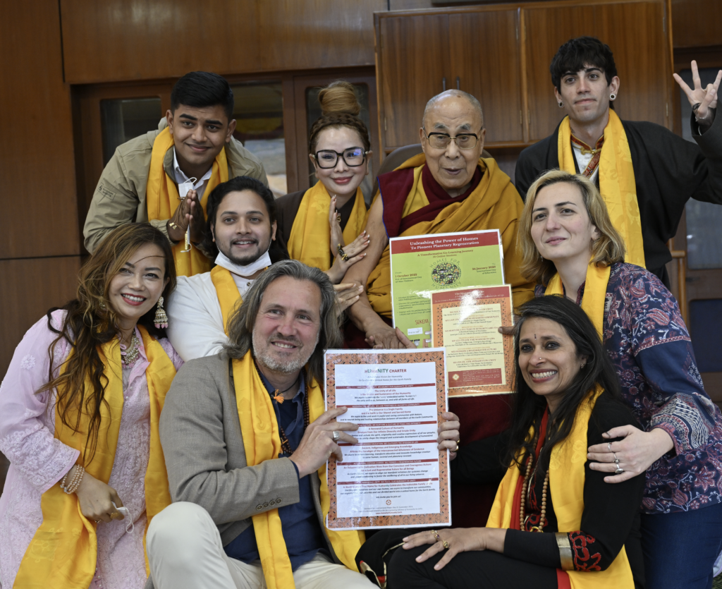 Dr. Tibet stands in a group of people, including the Dalai Lama, wearing the orange scarves of Buddhist monks. They are holding up several documents for the camera.