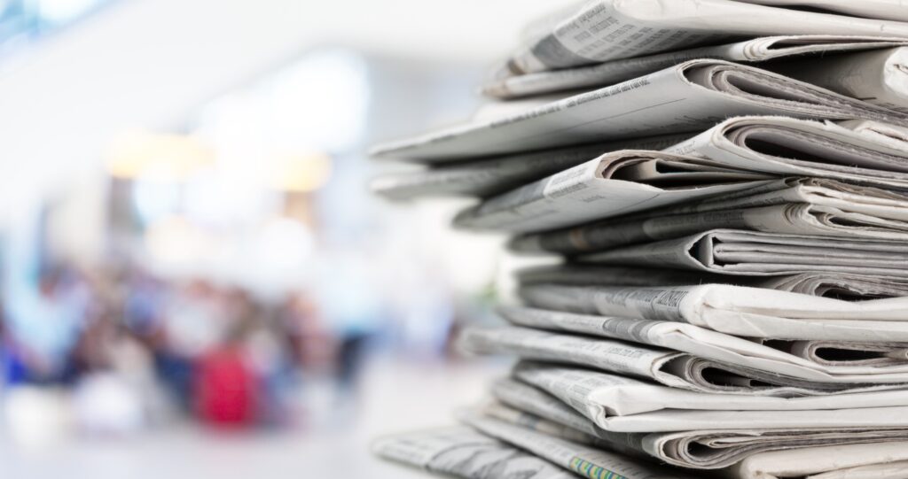 A stack of newspapers in front of a blurred background, representing journalism fellowships.