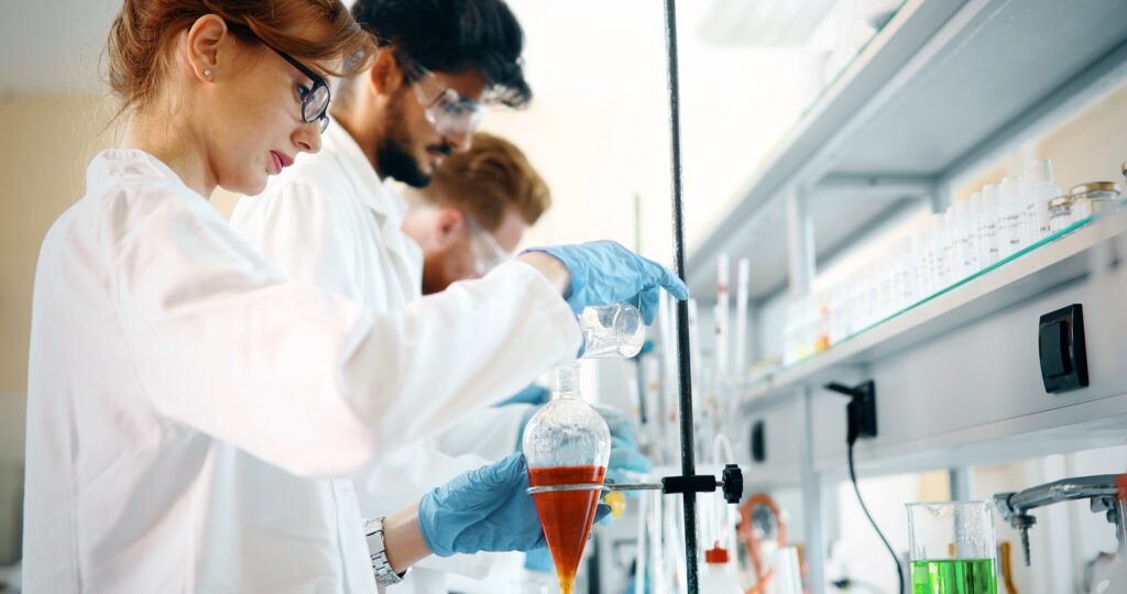 Group of chemistry students working in laboratory wearing lab coats, goggles, and handling solutions in glassware. This image represents the upcoming fellowship deadlines for a fully funded PhD in Chemical Engineering.